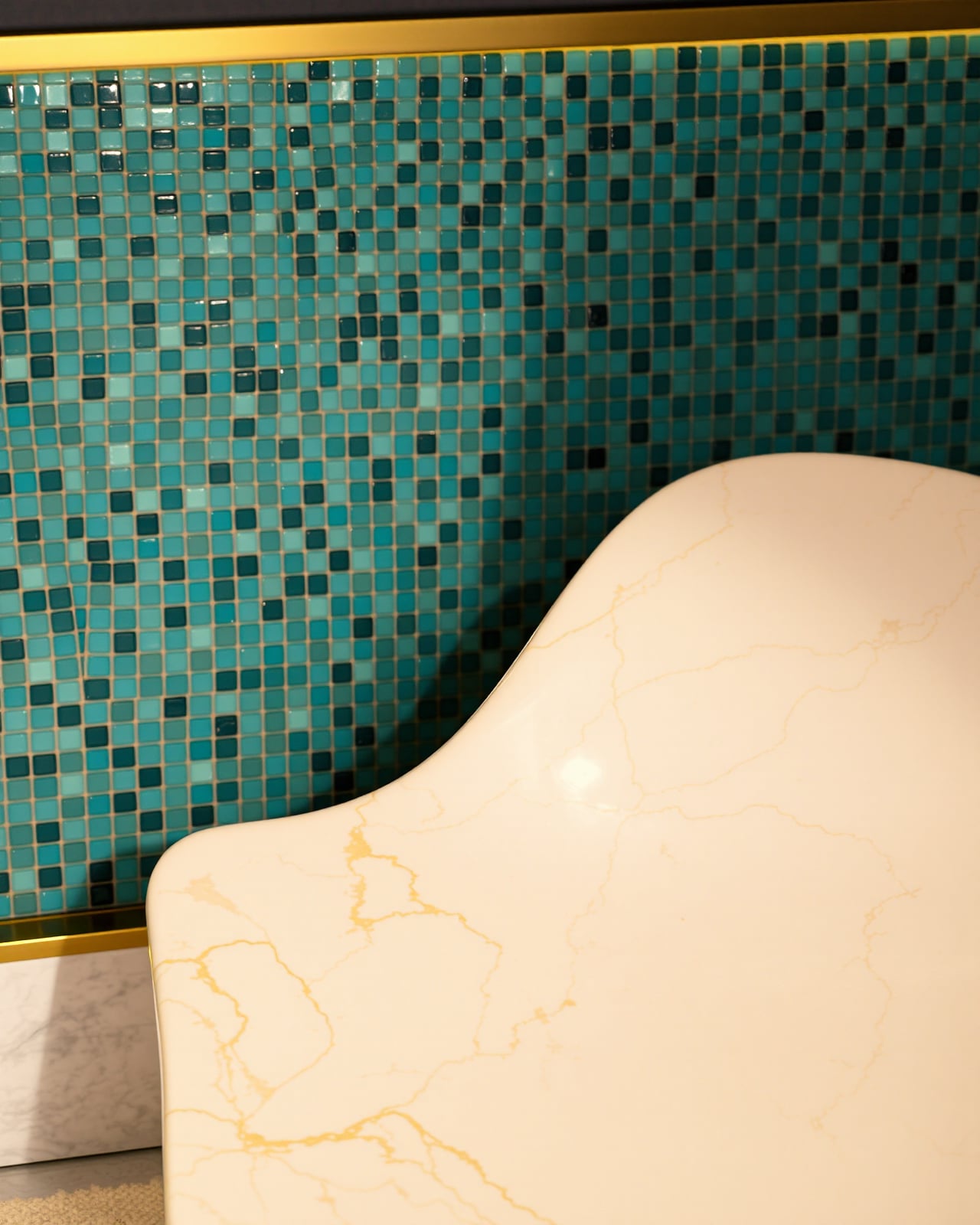 A single contoured heated-marble lounger, its sculpted backrest catching candlelight against a wall of jewel-teal glass mosaic with gold grout.